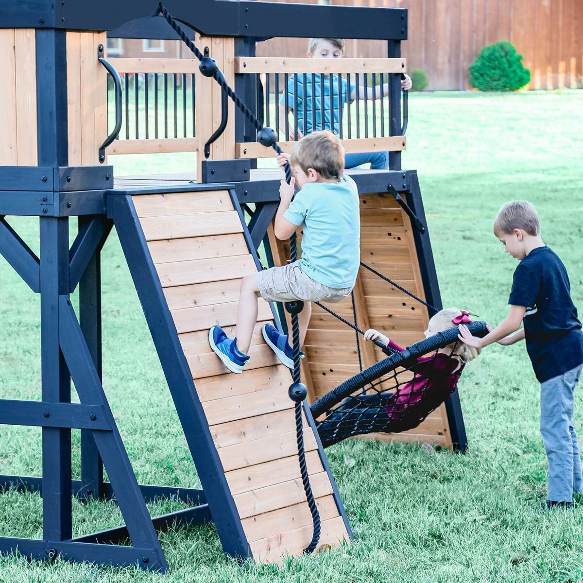 Lifestyle image of a child climbing the wall, and two children using the web swing Lifestyle image of a child climbing the wall, and two children using the web swing