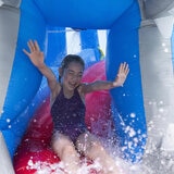 Lifestyle image of a child sliding out the mouth of the whale as water sprays on them Lifestyle image of a child sliding out the mouth of the whale as water sprays on them